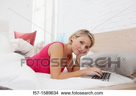Young woman relaxing on her bed on a laptop View Large Photo Image Picture - Young woman relaxing on her bed on a laptop. Fotosearch
