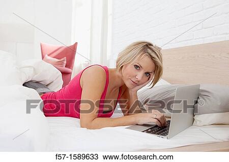 Young woman relaxing on her bed on a laptop View Large Photo Image Stock Image - Young woman relaxing on her bed on a laptop. Fotosearch