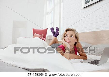 Young woman relaxing on her bed on a laptop View Large Photo Image Stock Image - Young woman relaxing on her bed on a laptop. Fotosearch