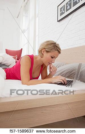 Young woman relaxing on her bed on a laptop View Large Photo Image Stock Photo - Young woman relaxing on her bed on a laptop. Fotosearch