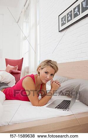 Young woman relaxing on her bed on a laptop View Large Photo Image Stock Photo - Young woman relaxing on her bed on a laptop. Fotosearch