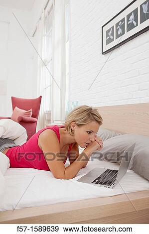 Young woman relaxing on her bed on a laptop View Large Photo Image Stock Photo - Young woman relaxing on her bed on a laptop. Fotosearch