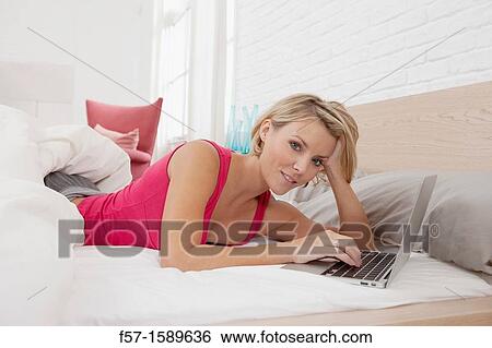 Young woman relaxing on her bed on a laptop View Large Photo Image Stock Photograph - Young woman relaxing on her bed on a laptop. Fotosearch