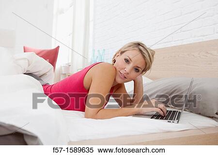Young woman relaxing on her bed on a laptop View Large Photo Image Stock Photography - Young woman relaxing on her bed on a laptop. Fotosearch