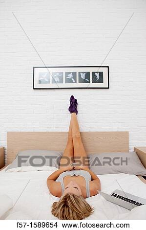 Young woman relaxing on her bed on her laptop View Large Photo Image Picture - Young woman relaxing on her bed on her laptop. Fotosearch