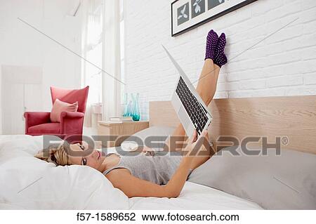 Young woman relaxing on her bed on her laptop View Large Photo Image Stock Image - Young woman relaxing on her bed on her laptop. Fotosearch