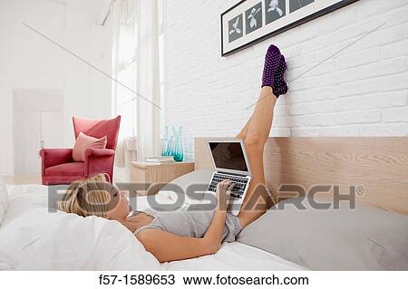 Young woman relaxing on her bed on her laptop View Large Photo Image Stock Image - Young woman relaxing on her bed on her laptop. Fotosearch