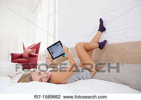 Young woman relaxing on her bed on her tablet computer View Large Photo Image Stock Image - Young woman relaxing on her bed on her tablet computer. Fotosearch