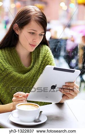 Stock Photo - Young woman relaxing with her Cappuccino while browsing with her iPad outdoor. Fotosearch