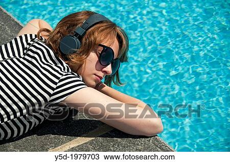 young woman resting at the poolside, listening to the music with headphones on View Large Photo Image Stock Image - young woman resting at the poolside, listening to the music with headphones on. Fotosearch