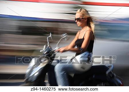 Stock Photography - Young woman riding scooter. Fotosearch