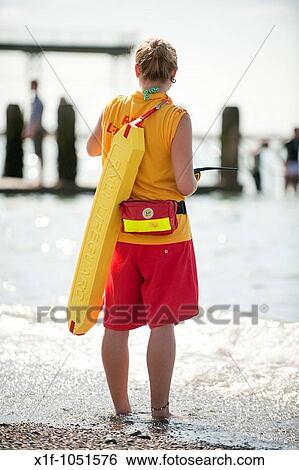 Stock Photograph - young woman RNLI lifeguard on duty, patrolling Aberystwyth beach, summer afternoon, Ceredigion Wales UK. Fotosearch