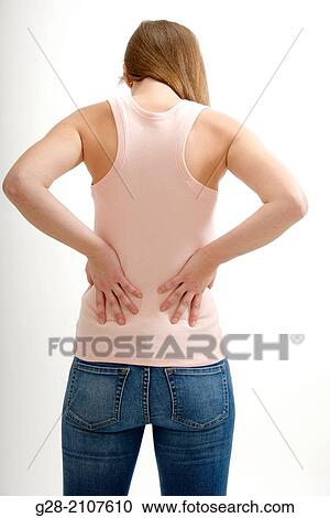 Stock Image - Young woman seen from behind holding her back for pain. Fotosearch