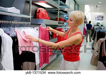 Picture - Young woman shopping and comparing different clothes in store. Fotosearch