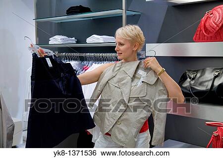 Stock Photograph - Young woman shopping and comparing different clothes in store. Fotosearch
