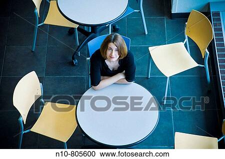 Young woman sitting at a table in a cafeteria. View Large Photo Image Stock Image - Young woman sitting at a table in a cafeteria.. Fotosearch