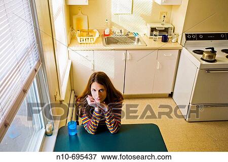 Young woman sitting at her kitchen table. View Large Photo Image Stock Photo - Young woman sitting at her kitchen table.. Fotosearch
