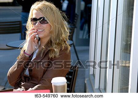 young woman sitting at outdoor cafe talking on cell phone View Large Photo Image Stock Image - young woman sitting at outdoor cafe talking on cell phone. Fotosearch