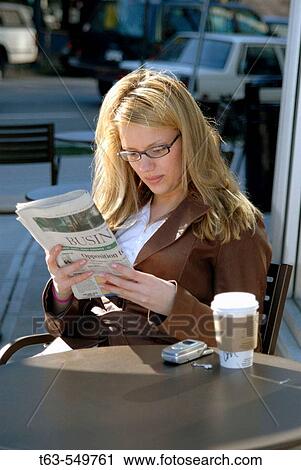 Stock Image - young woman sitting at outdoor cafe reading newspaper. Fotosearch