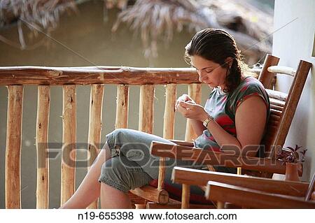 Stock Photo - Young woman sitting in chair near river. Fotosearch