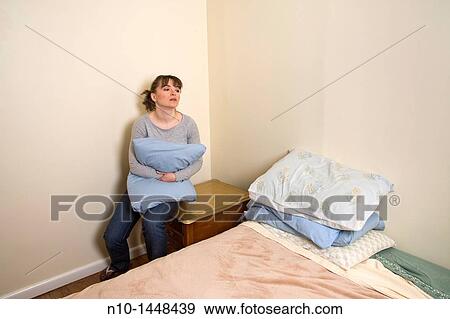 Stock Photo - Young woman sitting next to her bed. Fotosearch