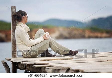 Picture - Young woman sitting on a bridge.. Fotosearch
