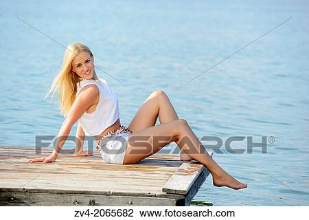 Stock Image - Young woman sitting on a jetty at a lake in Austria.. Fotosearch