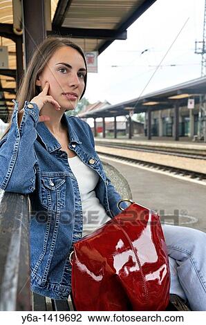 Stock Image - Young woman sitting on bench at railroad station. Fotosearch