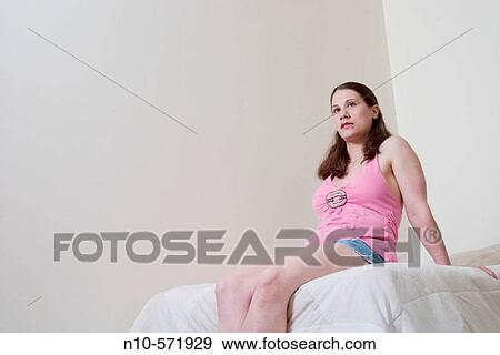 Young woman sitting on her bed View Large Photo Image Stock Photo - Young woman sitting on her bed. Fotosearch