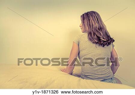 Stock Photograph - Young woman sitting on her bed. Fotosearch