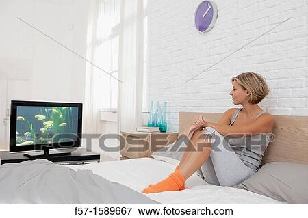 Young woman sitting on her bed watching TV View Large Photo Image Stock Photo - Young woman sitting on her bed watching TV. Fotosearch