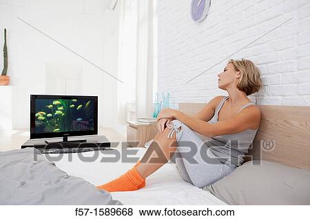 Young woman sitting on her bed watching TV View Large Photo Image Stock Photo - Young woman sitting on her bed watching TV. Fotosearch