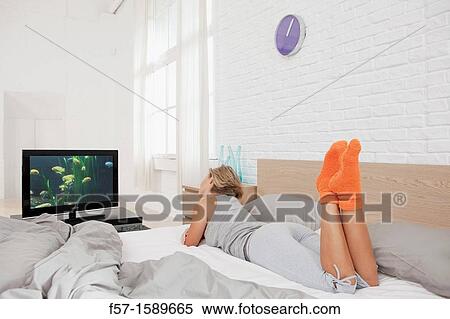 Stock Photography - Young woman sitting on her bed watching TV. Fotosearch