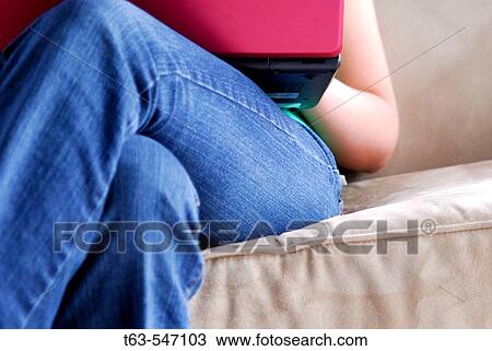 Stock Image - young woman sitting on sofa using laptop computer. Fotosearch
