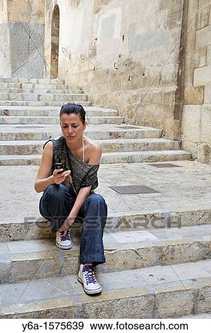 Stock Photo - Young woman sitting on stairs outdoors text messaging. Fotosearch