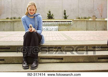 Young woman sitting on steps with cell phone View Large Photo Image Picture - Young woman sitting on steps with cell phone. Fotosearch