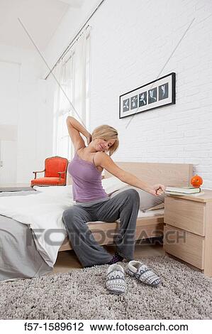 Young woman sitting on the edge of her bed stretching View Large Photo Image Stock Image - Young woman sitting on the edge of her bed stretching. Fotosearch
