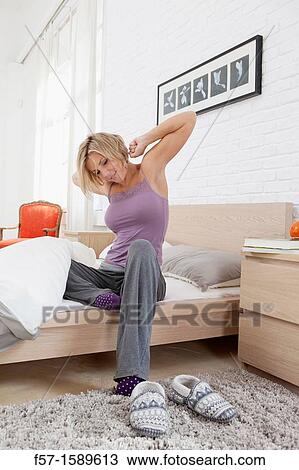 Young woman sitting on the edge of her bed stretching View Large Photo Image Stock Image - Young woman sitting on the edge of her bed stretching. Fotosearch