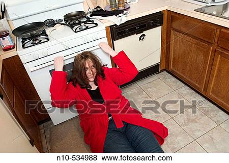 Stock Photo - Young woman sitting on the floor of her kitchen. Fotosearch