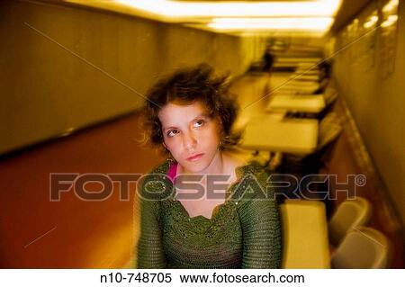 Stock Photography - Young woman sitting on top of a table in front of several empty tables.. Fotosearch