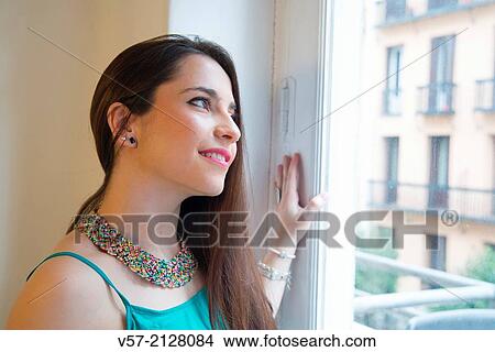 Young woman smiling and looking through a window. View Large Photo Image Picture - Young woman smiling and looking through a window.. Fotosearch