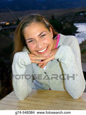 Young woman smiling at a table View Large Photo Image Picture - Young woman smiling at a table. Fotosearch
