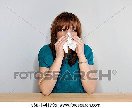 Stock Photography - Young woman sneezing and blowing nose with white tissue. Fotosearch