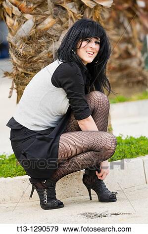 Young woman squatting on street and adjusting her shoe View Large Photo Image Stock Photo - Young woman squatting on street and adjusting her shoe. Fotosearch
