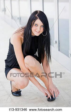 Stock Photograph - Young woman squatting on street and adjusting her shoe. Fotosearch