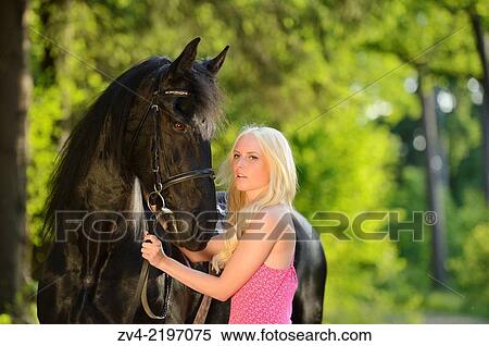 Stock Photography - Young woman standing beside a Friesian horse in late sunlight.. Fotosearch
