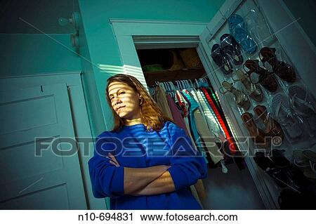 Stock Image - Young woman standing by her clothes closet in her bedroom. Fotosearch