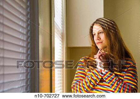 Young woman standing by her window. View Large Photo Image Stock Photo - Young woman standing by her window.. Fotosearch