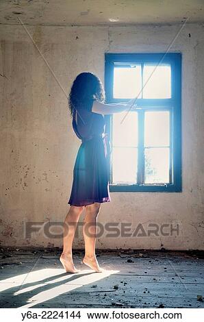 Young woman standing by the window reaching for the light. View Large Photo Image Picture - Young woman standing by the window reaching for the light.. Fotosearch