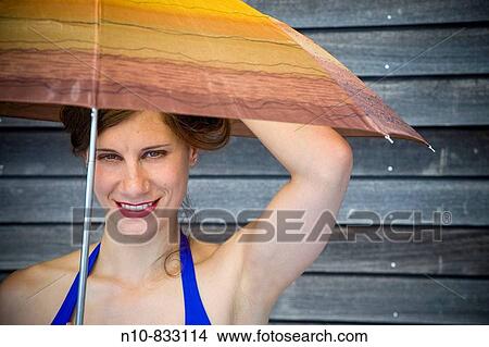 Picture - Young woman, standing in front of a wood building, holding an umbrella.. Fotosearch